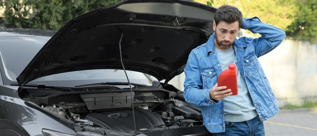 Man looking at bottle of motor oil leaning against car