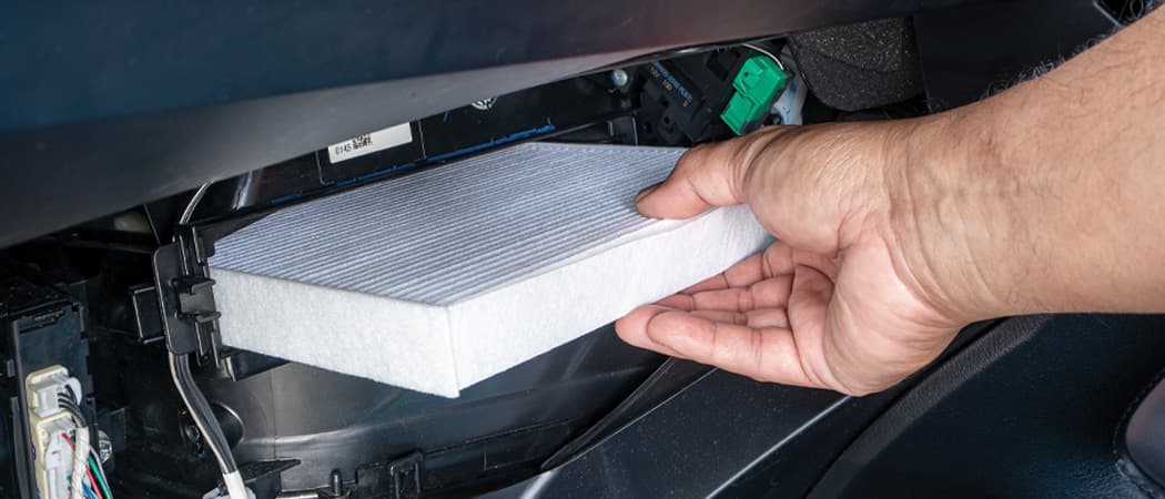 Technician replacing a car's cabin air filter, via a panel behind the glove compartment.